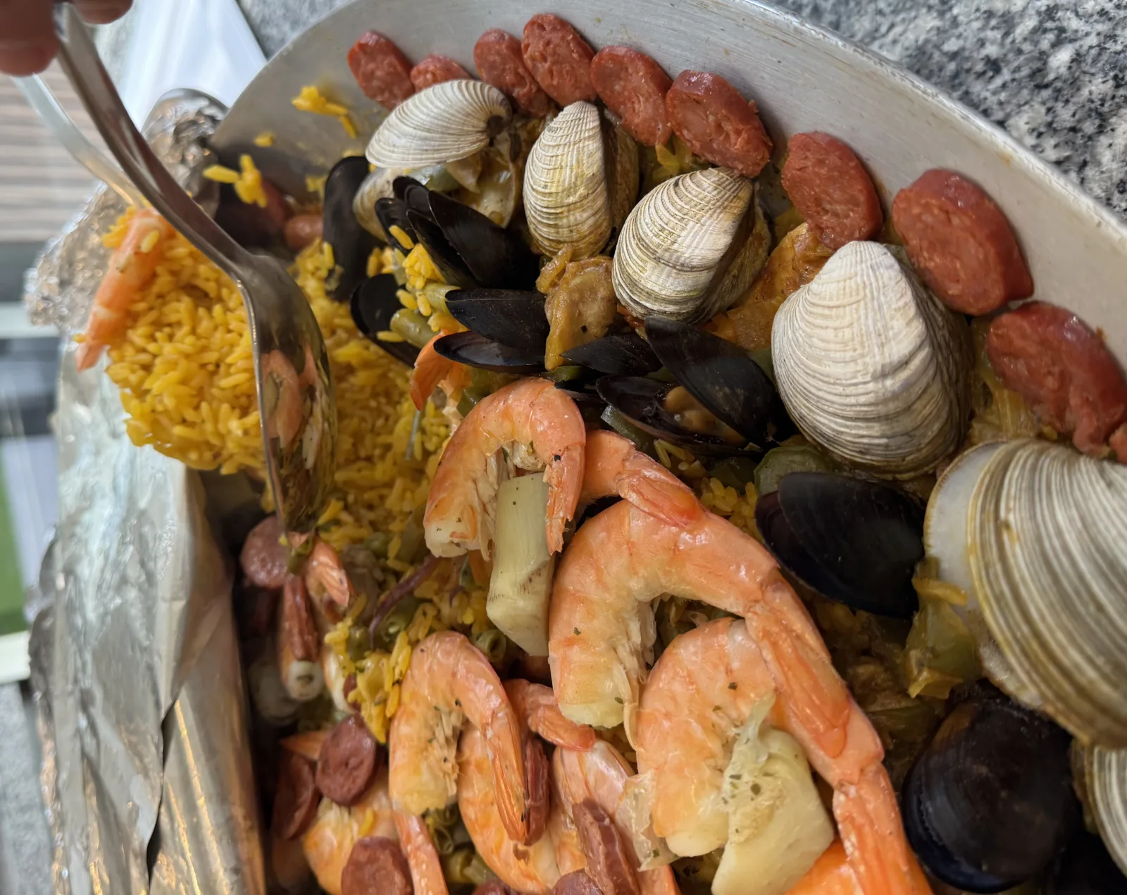 Sirviendo arroz a la paella marinera con una cuchara, con almejas, mejillones, camarón y chorizo alrededor
