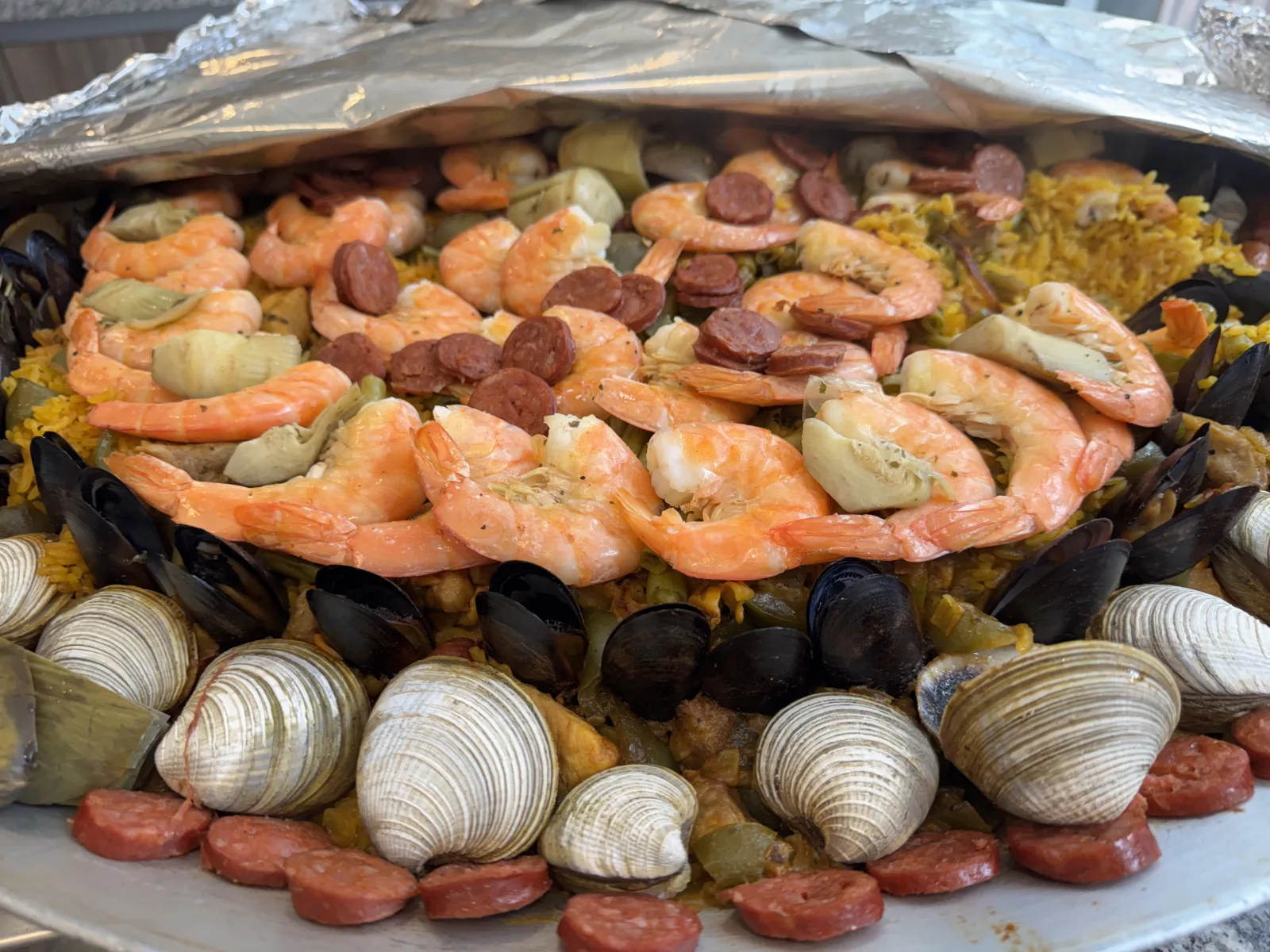 Paella marinera recién sacada del papel aluminio, con camarón, mejillón, almeja y chorizo sobre arroz amarillo