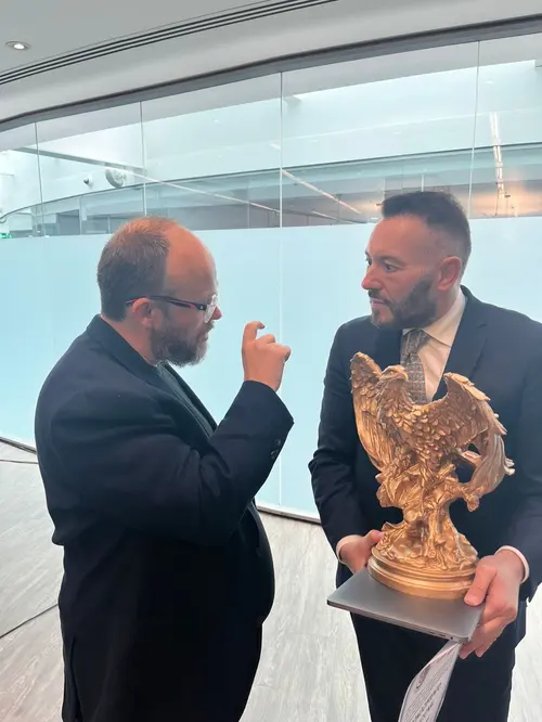 Esteban Rey sostiene un trofeo dorado en una oficina moderna con un colega.