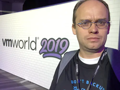 Esteban posa serio frente a un panel de VMworld 2019 con su característico bigote y una camiseta que pone DON'T BACKUP.